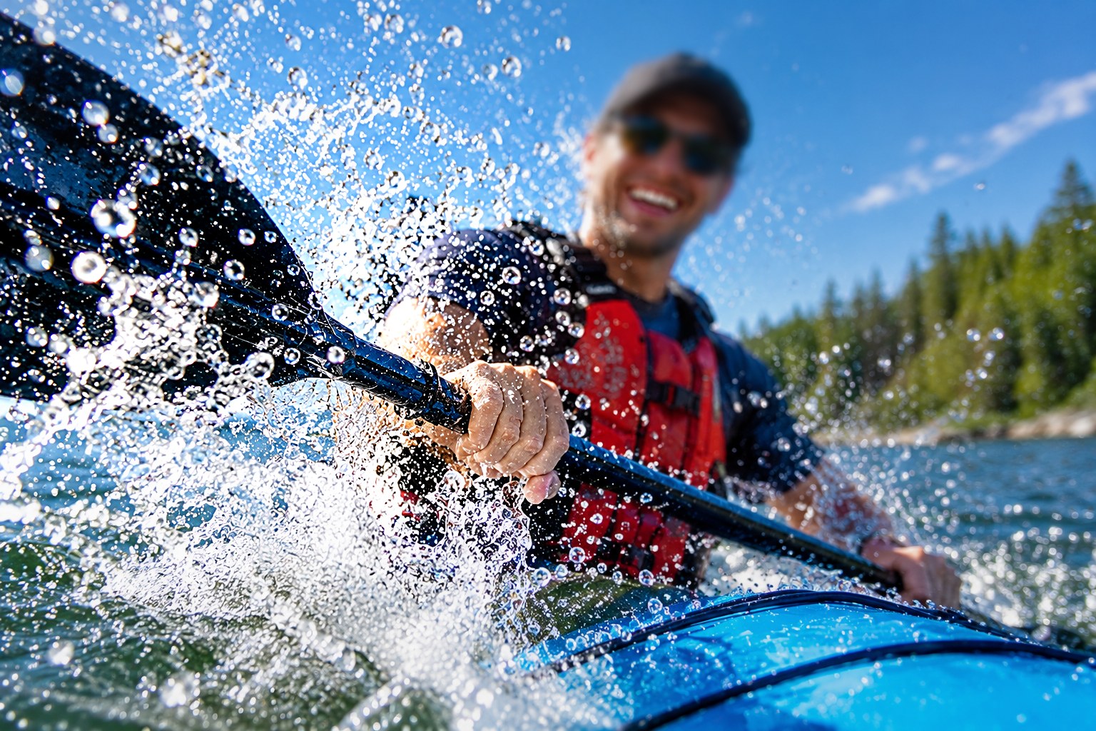 A smiling paddler in sunglasses drives a kayak paddle through a burst of splashing water